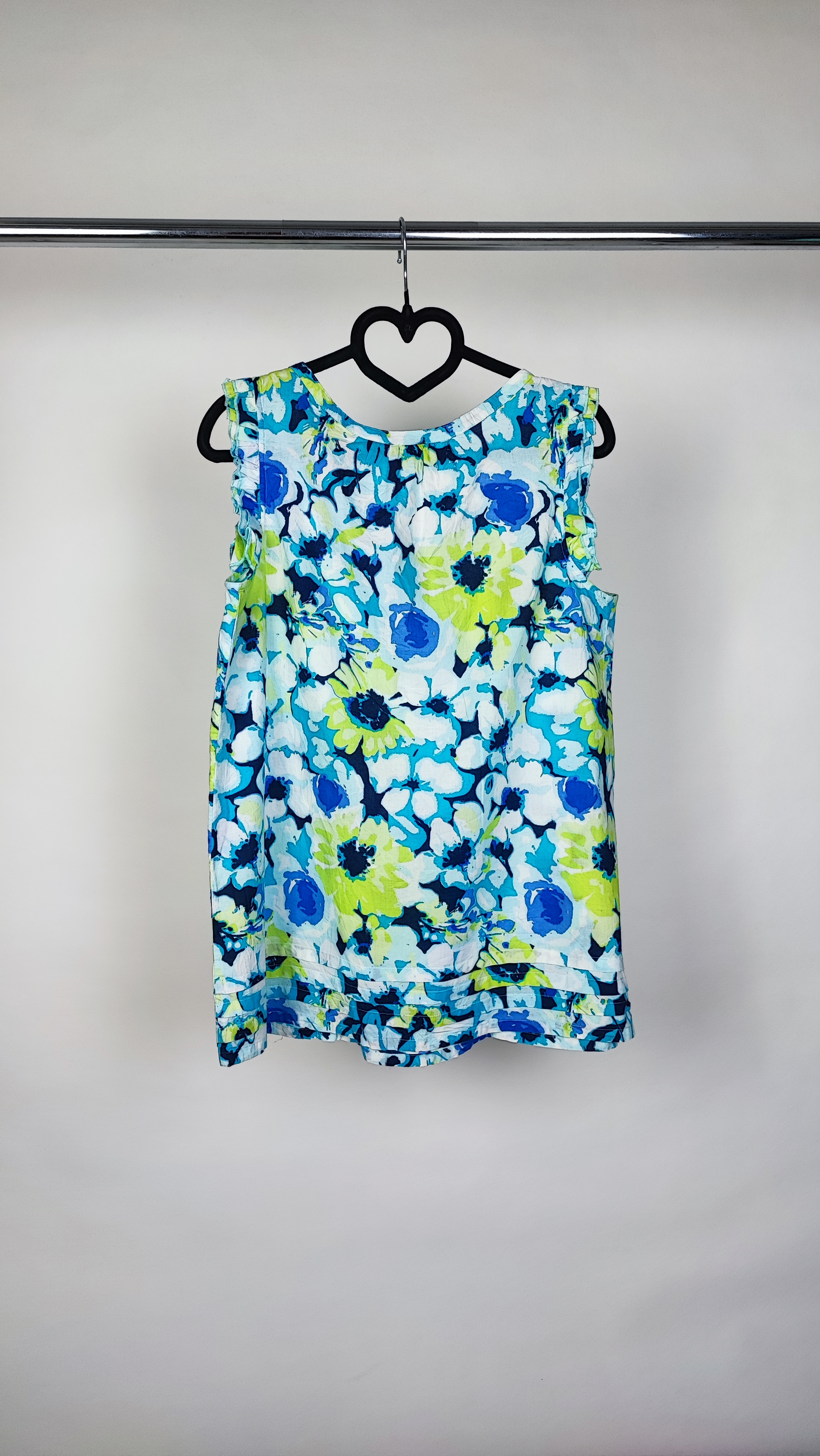 تصویر نیم‌قد زنی با تاپ بدون‌آستین طرح‌دار آبی‑سبز با زمینه روشن، در پس‌زمینه سفید.»