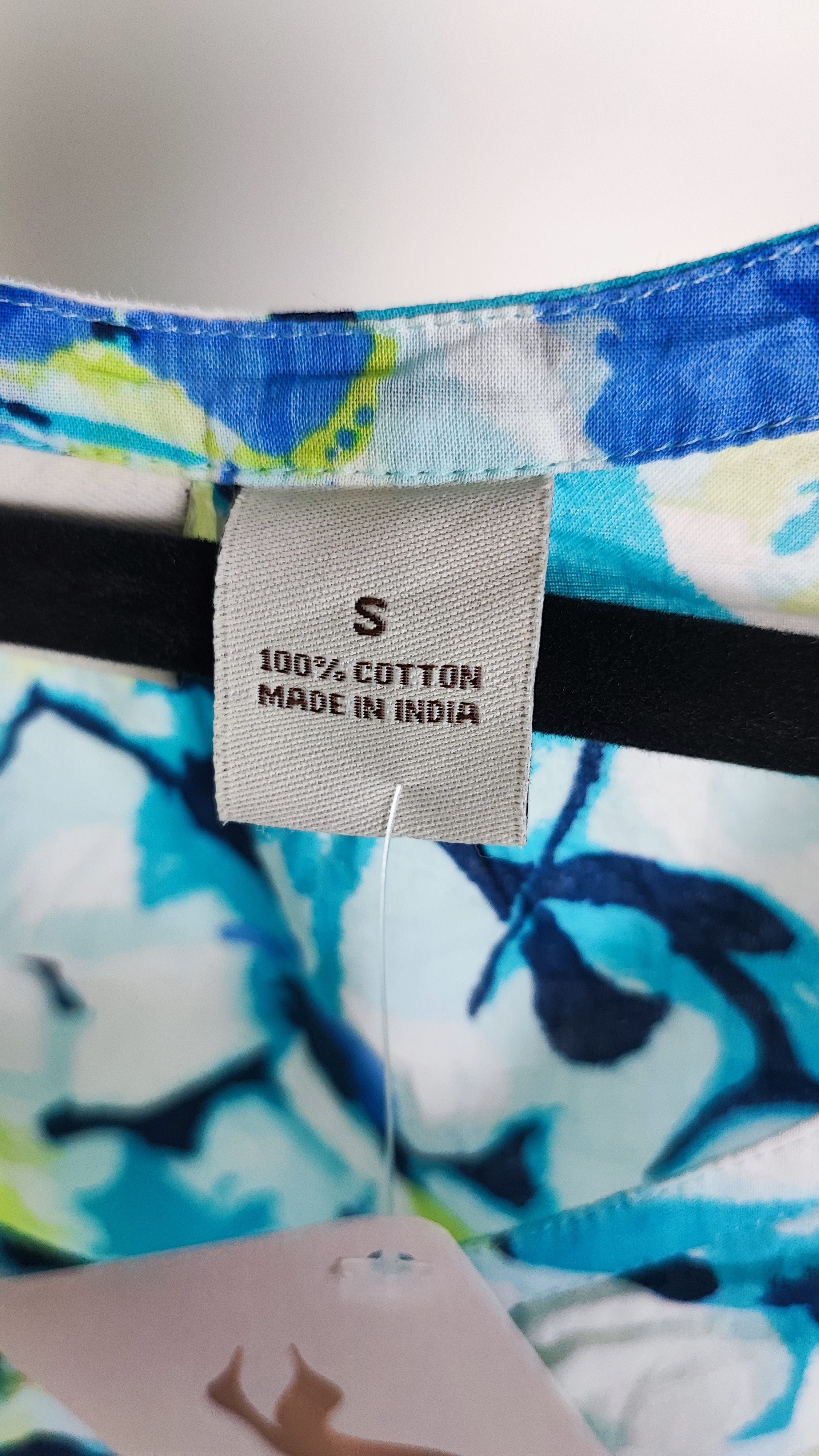 تصویر نیم‌قد زنی با تاپ بدون‌آستین طرح‌دار آبی‑سبز با زمینه روشن، در پس‌زمینه سفید.»