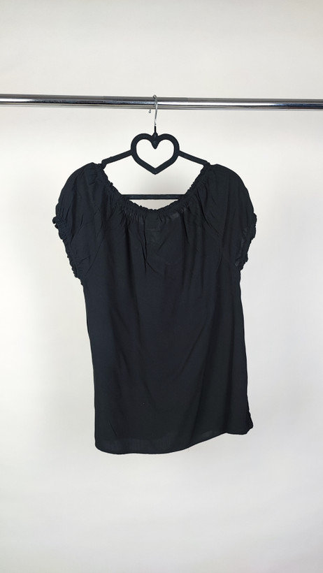 تصویر نیمتنه یک زن که شومیز مشکی آستینکوتاه پوشیده است. یقه گرد با نواردار دارد و جلوی لباس یک چین عمودی دیده میشود. پسزمینه ساده و روشن است.»