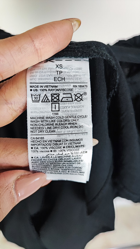 تصویر نیمتنه یک زن که شومیز مشکی آستینکوتاه پوشیده است. یقه گرد با نواردار دارد و جلوی لباس یک چین عمودی دیده میشود. پسزمینه ساده و روشن است.»