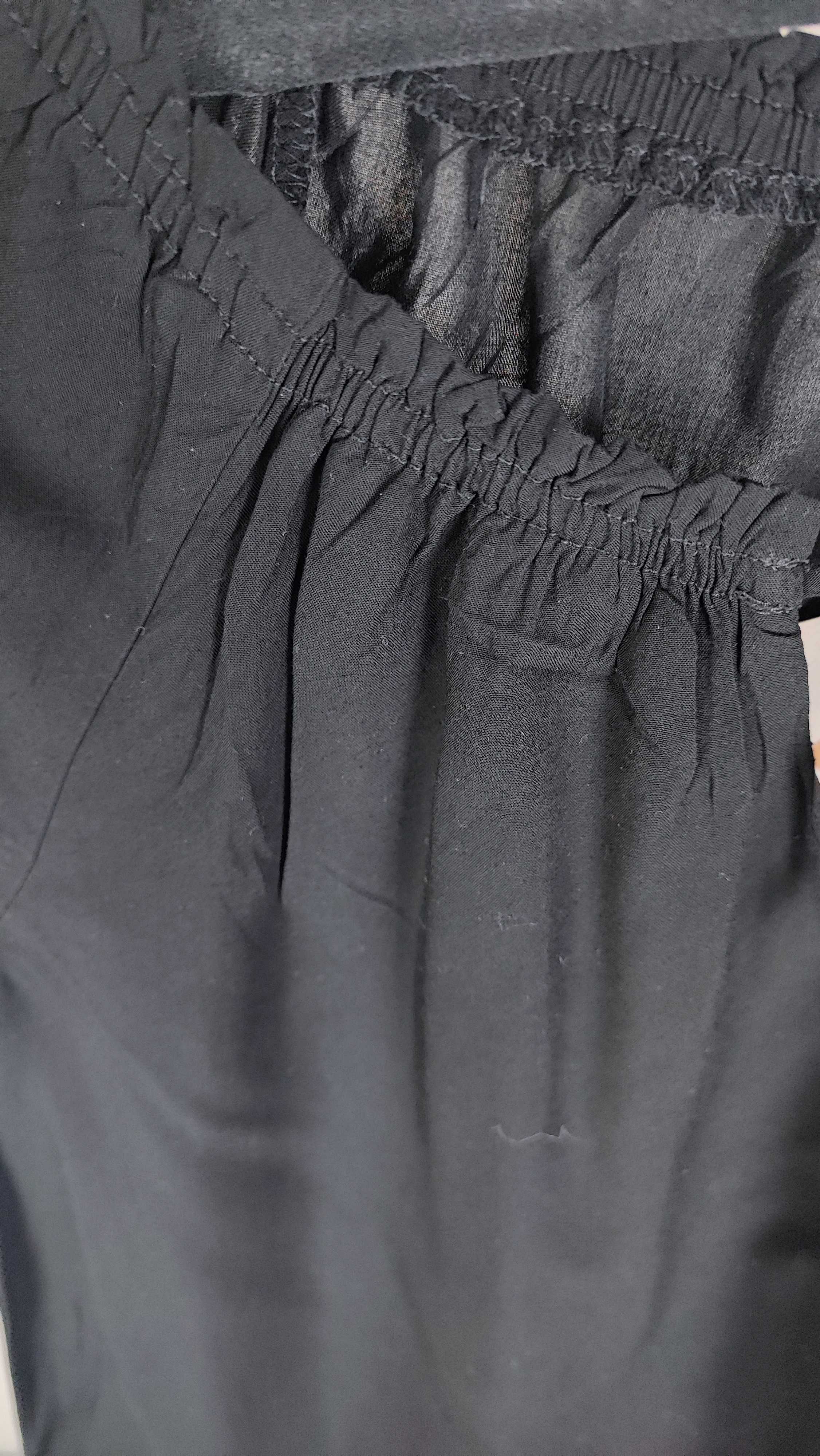 تصویر نیم‌تنه یک زن که شومیز مشکی آستین‌کوتاه پوشیده است. یقه گرد با نواردار دارد و جلوی لباس یک چین عمودی دیده می‌شود. پس‌زمینه ساده و روشن است.»