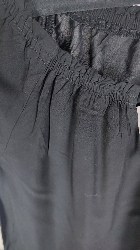 تصویر نیمتنه یک زن که شومیز مشکی آستینکوتاه پوشیده است. یقه گرد با نواردار دارد و جلوی لباس یک چین عمودی دیده میشود. پسزمینه ساده و روشن است.»