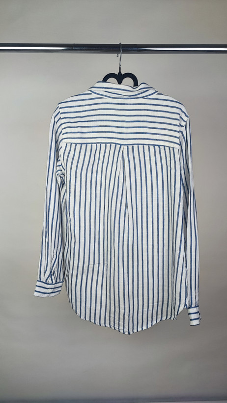 تصویر نیمتنه زنی با شومیز آستینبلند راهراه عمودی آبی و سفید، با یقهدار و فرم نیمهراسته. پسزمینه روشن و ساده است.»