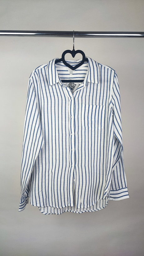 تصویر نیمتنه زنی با شومیز آستینبلند راهراه عمودی آبی و سفید، با یقهدار و فرم نیمهراسته. پسزمینه روشن و ساده است.»