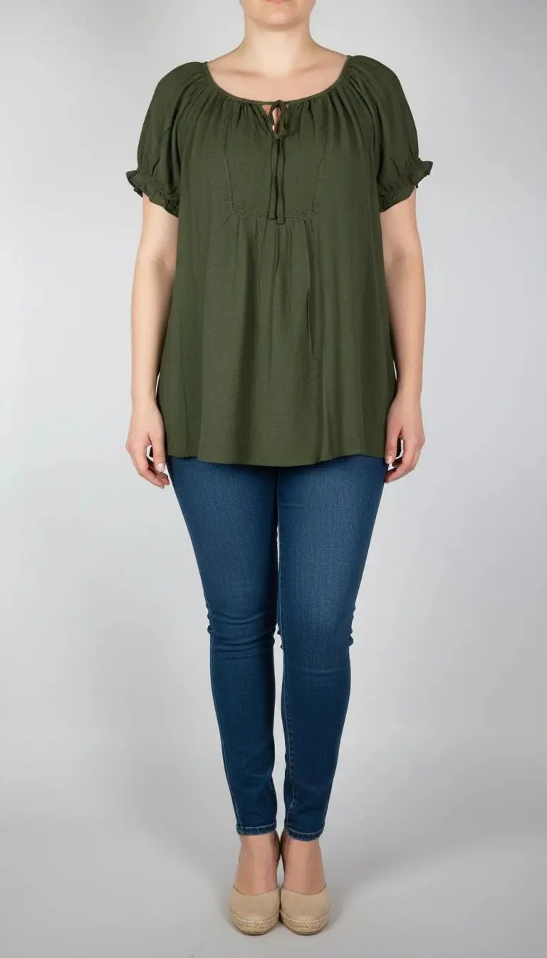 تصویر تمام‌قد زنی با شومیز سبز تیره آستین‌کوتاه و فرم آزاد که با شلوار جین تیره ست شده است. یقه گرد و پارچه سبک دارد