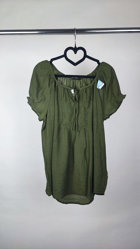 تصویر تمامقد زنی با شومیز سبز تیره آستینکوتاه و فرم آزاد که با شلوار جین تیره ست شده است. یقه گرد و پارچه سبک دارد