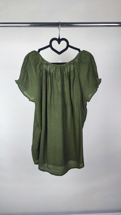 تصویر تمامقد زنی با شومیز سبز تیره آستینکوتاه و فرم آزاد که با شلوار جین تیره ست شده است. یقه گرد و پارچه سبک دارد