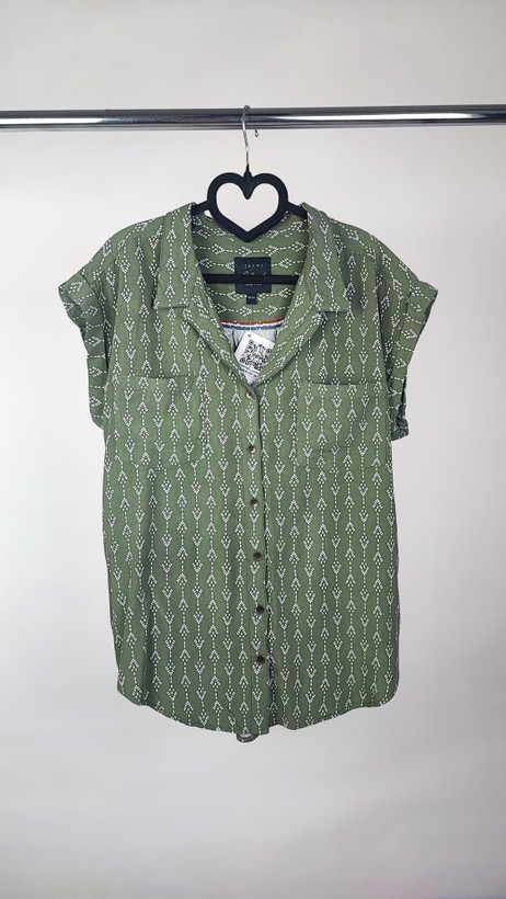 تصویر تمامقد زنی با شومیز سبز یشمی با یقه هفت و آستین کوتاه، ستشده با شلوار جین تیره. پسزمینه سفید و ساده است.»