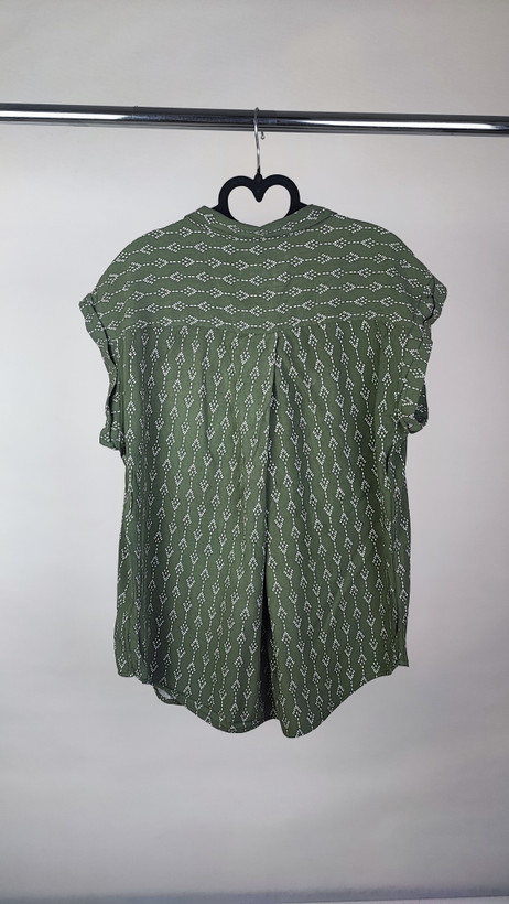 تصویر تمامقد زنی با شومیز سبز یشمی با یقه هفت و آستین کوتاه، ستشده با شلوار جین تیره. پسزمینه سفید و ساده است.»