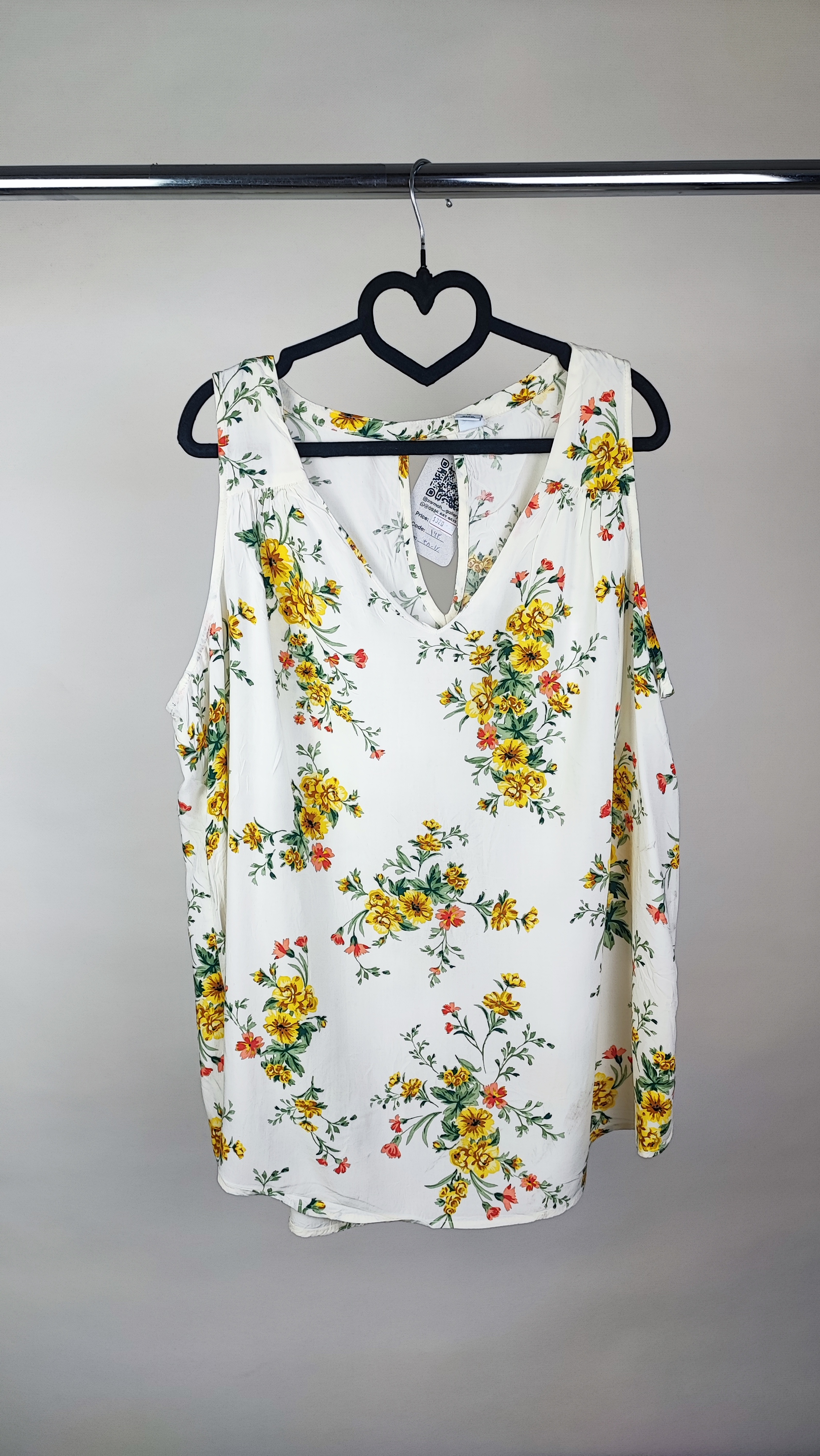 تصویر تمام‌قد زنی با تاپ بدون‌آستین روشنِ طرح‌دار با یقه هفت، ست‌شده با شلوار جین تیره. پس‌زمینه سفید و ساده است