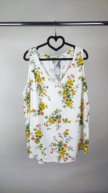 تصویر تمامقد زنی با تاپ بدونآستین روشنِ طرحدار با یقه هفت، ستشده با شلوار جین تیره. پسزمینه سفید و ساده است