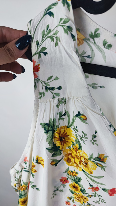 تصویر تمامقد زنی با تاپ بدونآستین روشنِ طرحدار با یقه هفت، ستشده با شلوار جین تیره. پسزمینه سفید و ساده است