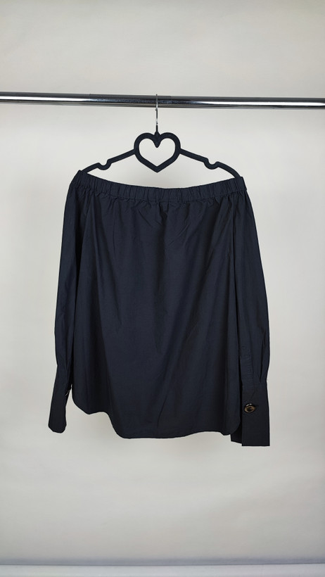 تصویر تمامقد زنی با شومیز مشکی آفشولدر (یقه باز روی شانه) و آستین بلند، ستشده با شلوار مشکی در پسزمینه سفید.»