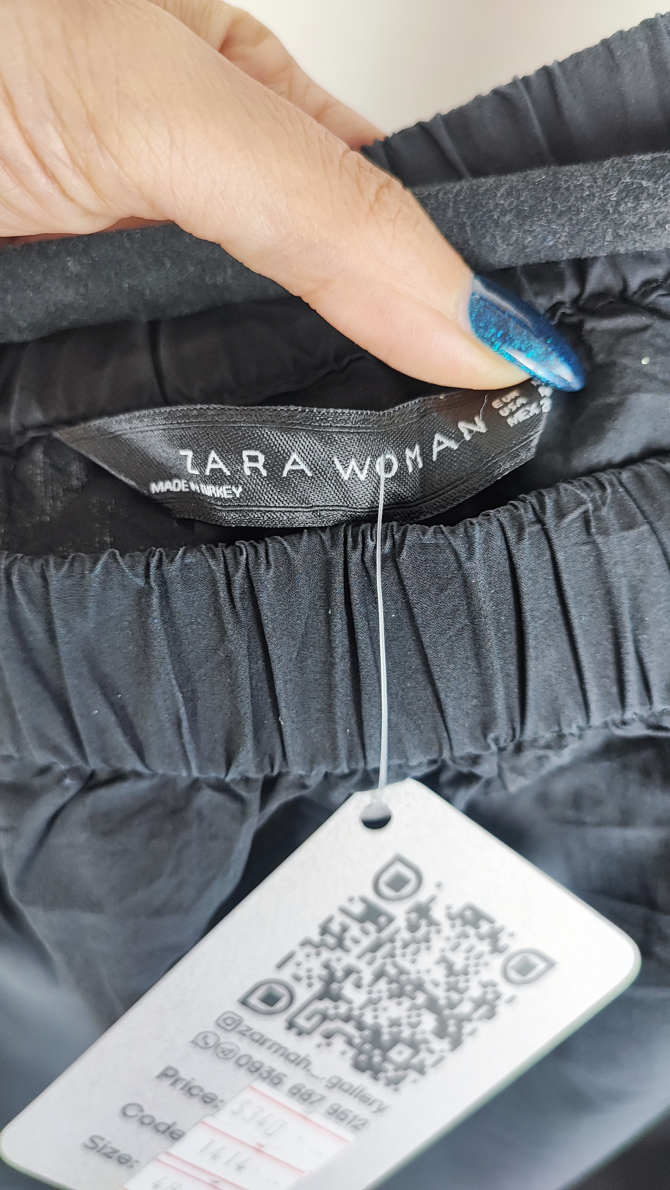 تصویر تمام‌قد زنی با شومیز مشکی آف‌شولدر (یقه باز روی شانه) و آستین بلند، ست‌شده با شلوار مشکی در پس‌زمینه سفید.»