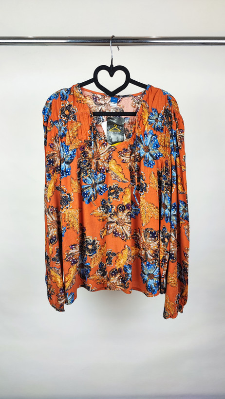 تصویر تمامقد زنی با شومیز سایز بزرگ طرحدار در تنالیته نارنجی و آبی با یقه هفت و آستینبلند، ستشده با شلوار تیره در پسزمینه ساده.»