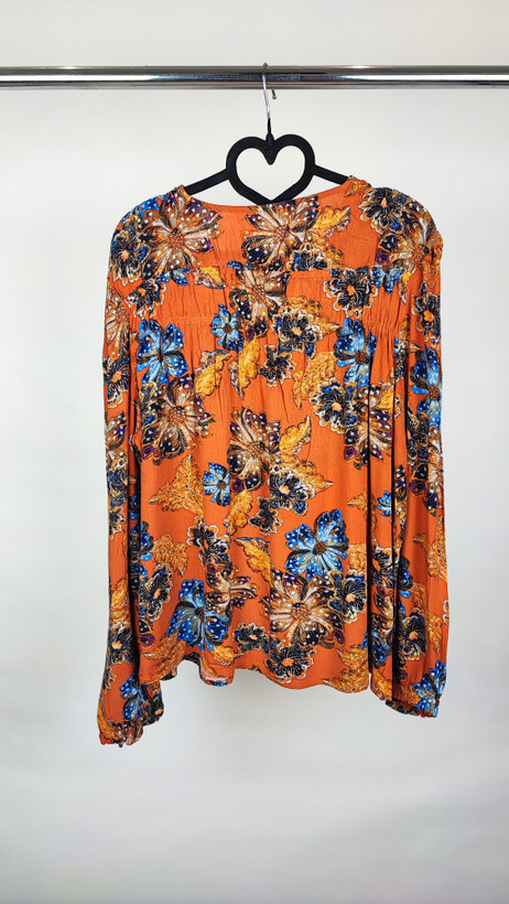 تصویر تمامقد زنی با شومیز سایز بزرگ طرحدار در تنالیته نارنجی و آبی با یقه هفت و آستینبلند، ستشده با شلوار تیره در پسزمینه ساده.»