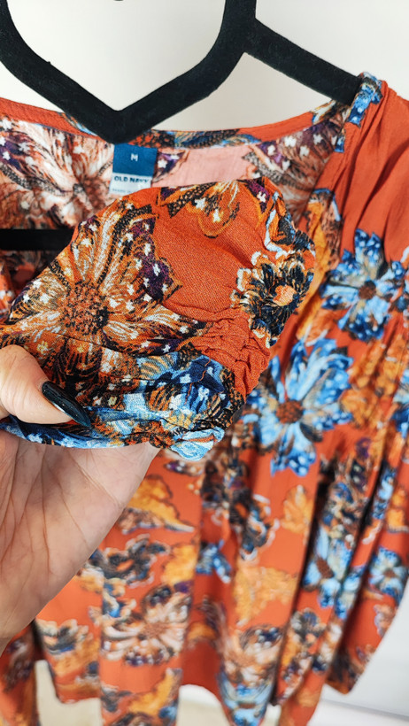 تصویر تمامقد زنی با شومیز سایز بزرگ طرحدار در تنالیته نارنجی و آبی با یقه هفت و آستینبلند، ستشده با شلوار تیره در پسزمینه ساده.»