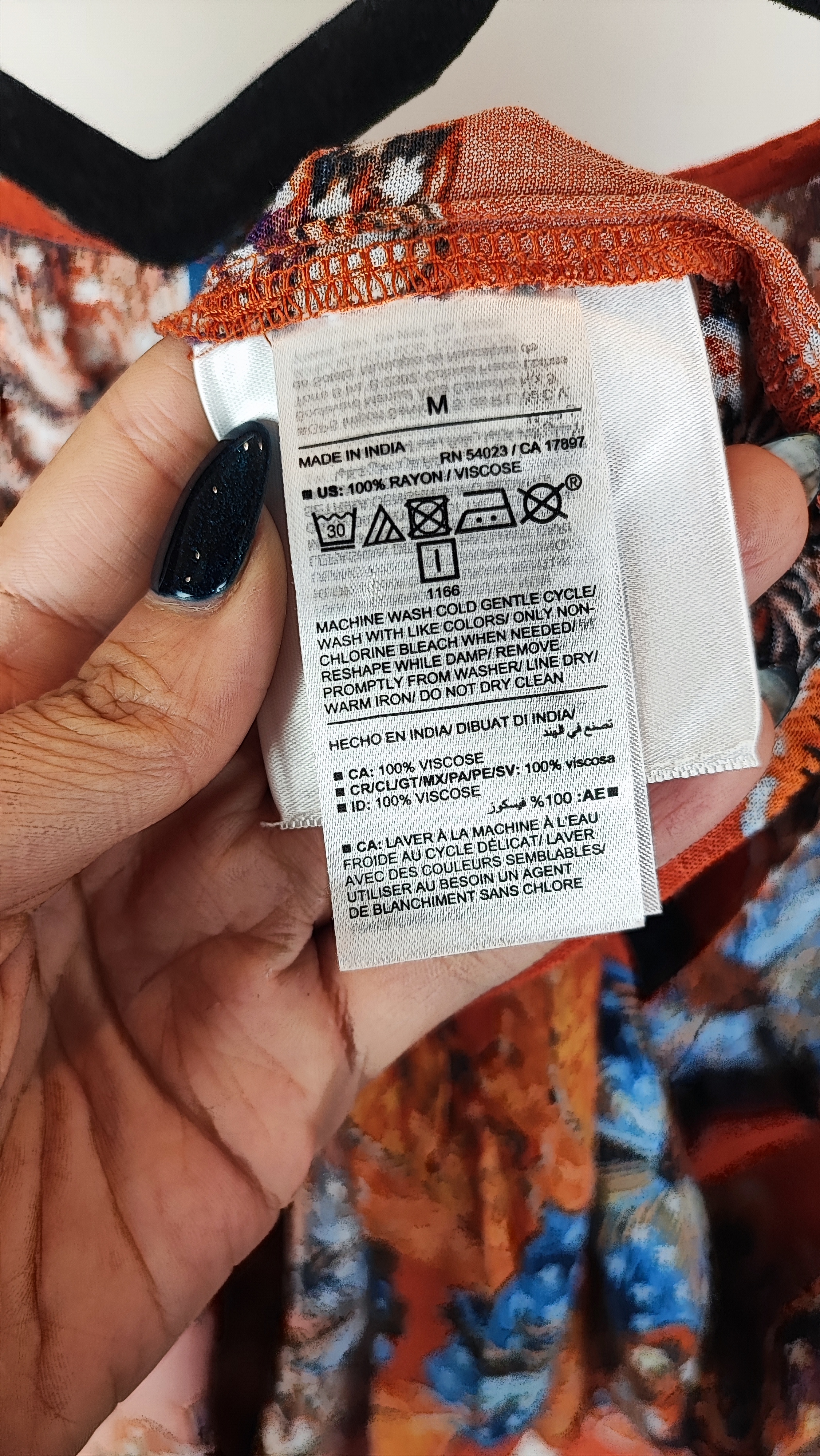 تصویر تمام‌قد زنی با شومیز سایز بزرگ طرح‌دار در تنالیته نارنجی و آبی با یقه هفت و آستین‌بلند، ست‌شده با شلوار تیره در پس‌زمینه ساده.»