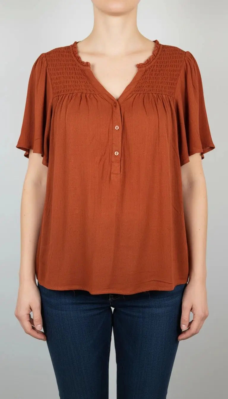 «تصویر نیم‌قد زنی با شومیز آستین‌کوتاه قهوه‌ای مایل به آجری با یقه هفت و برش ساده، ست‌شده با شلوار جین در پس‌زمینه روشن