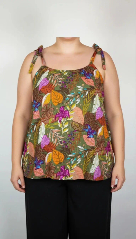 زن با تاپ بندی سایز بزرگ با طرح گلها و برگهای رنگی در تنالیته سبز، بنفش و زرد دیده میشود. فرم لباس آزاد است و با شلوار مشکی ست شده.»