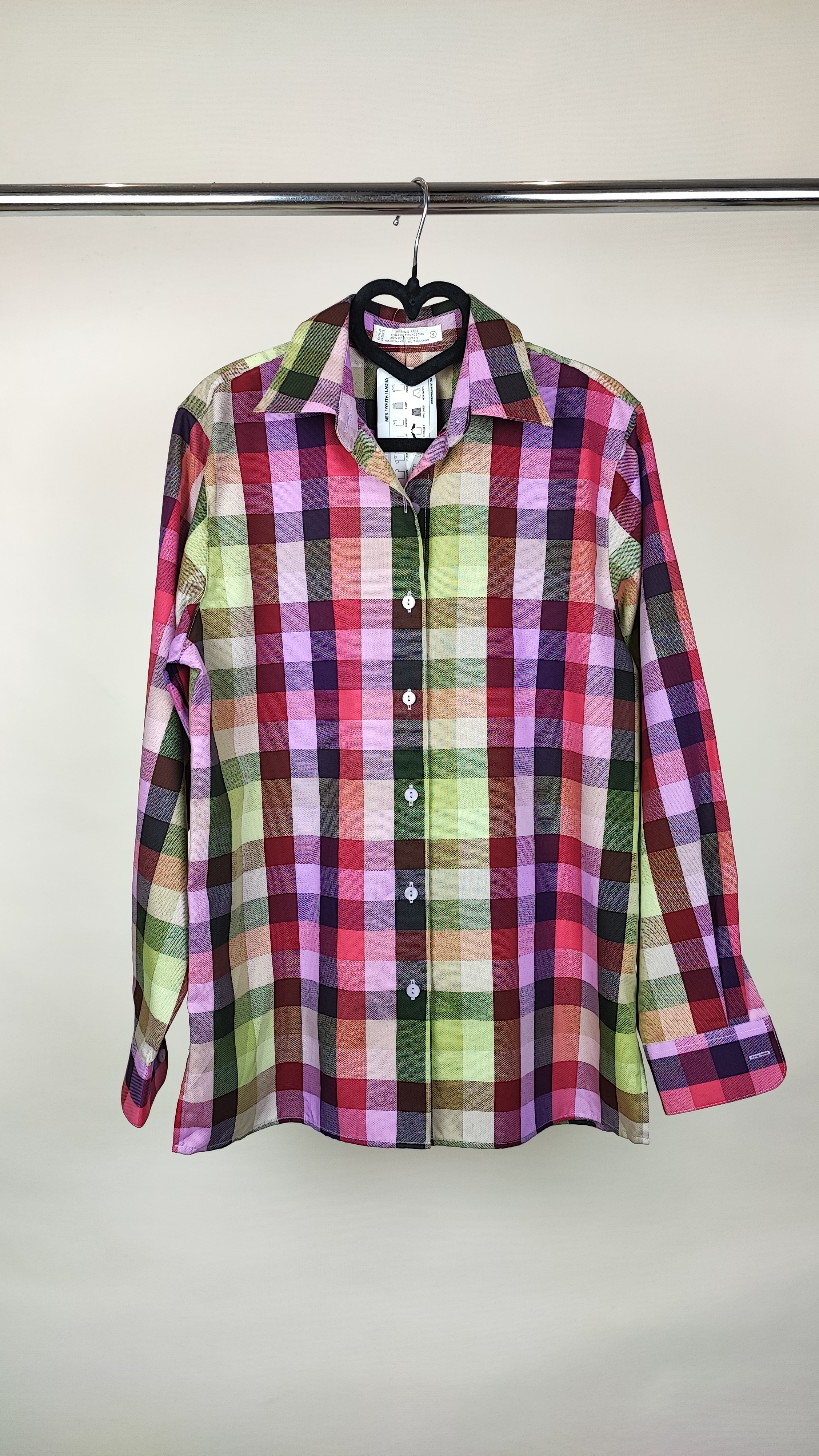 زن با شومیز چهارخونه آستین‌بلند در ترکیب رنگی صورتی، سبز و کرم دیده می‌شود. یقه برگردان و فرم لباس معمولی است و با شلوار جین تیره ست شده.»