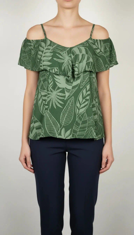 زن با بلوز سبز طرحدار مدل یقه باز و بندی دیده میشود. پارچه سبک و براق دارد، طرح آن برگ و گلهای درشت است، فرم لباس آزاد و راحت است و با شلوار مشکی ست شده.»