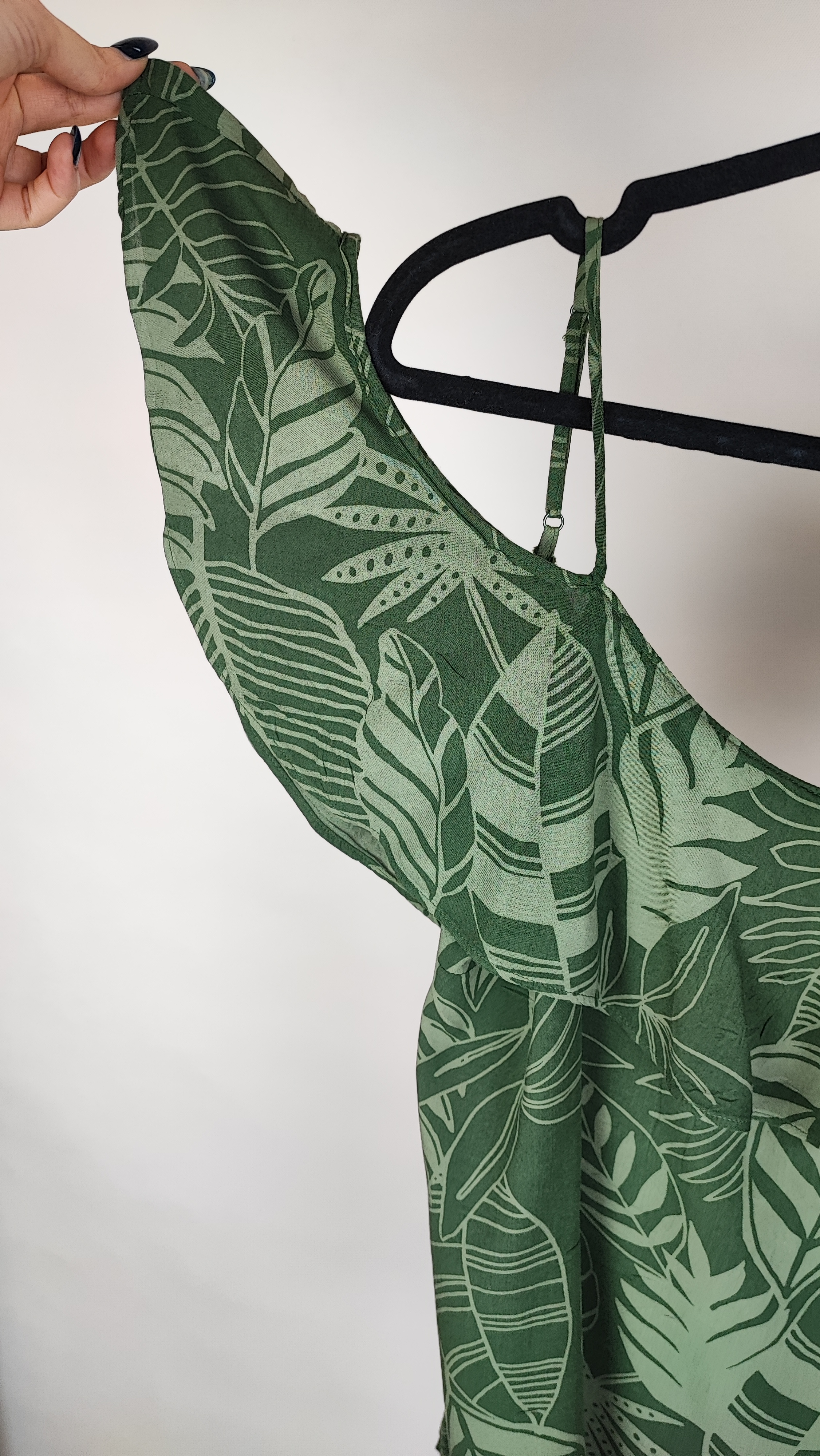 زن با بلوز سبز طرحدار مدل یقه باز و بندی دیده می‌شود. پارچه سبک و براق دارد، طرح آن برگ و گل‌های درشت است، فرم لباس آزاد و راحت است و با شلوار مشکی ست شده.»