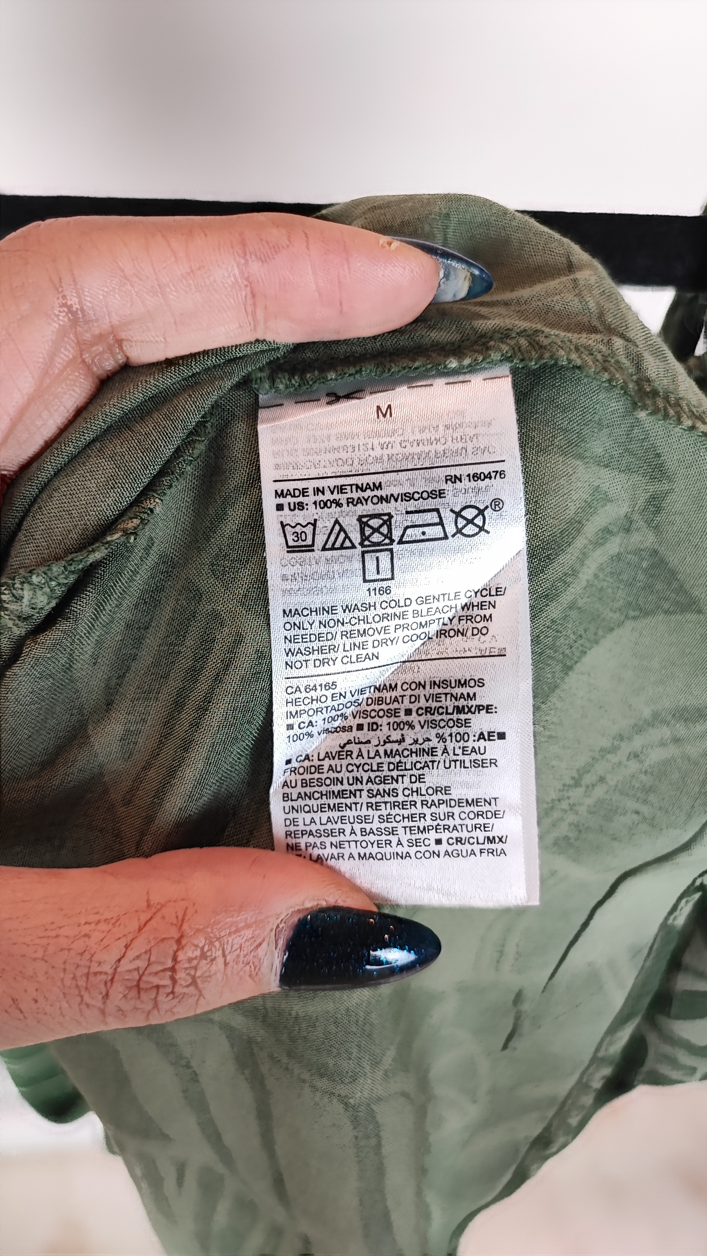 زن با بلوز سبز طرحدار مدل یقه باز و بندی دیده می‌شود. پارچه سبک و براق دارد، طرح آن برگ و گل‌های درشت است، فرم لباس آزاد و راحت است و با شلوار مشکی ست شده.»