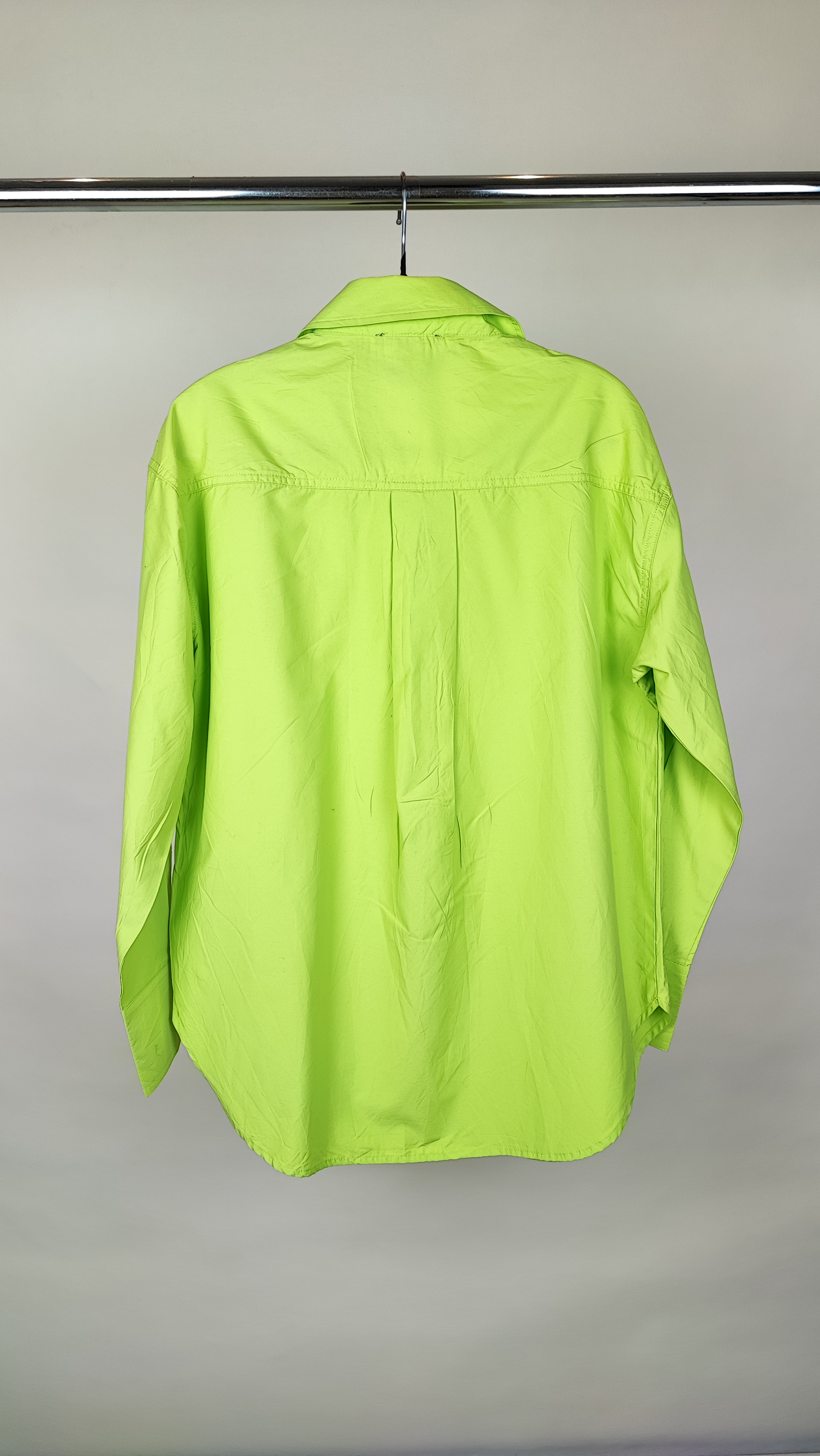 زن با شومیز لیمویی روشن آستین‌بلند و یقه برگردان دیده می‌شود. فرم لباس آزاد است و با شلوار جین تیره ست شده.»