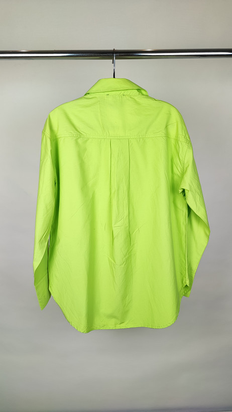 زن با شومیز لیمویی روشن آستینبلند و یقه برگردان دیده میشود. فرم لباس آزاد است و با شلوار جین تیره ست شده.»