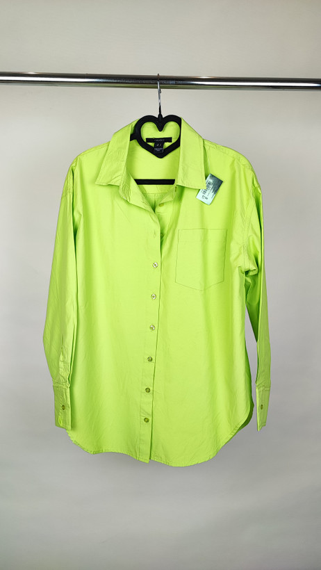 زن با شومیز لیمویی روشن آستینبلند و یقه برگردان دیده میشود. فرم لباس آزاد است و با شلوار جین تیره ست شده.»