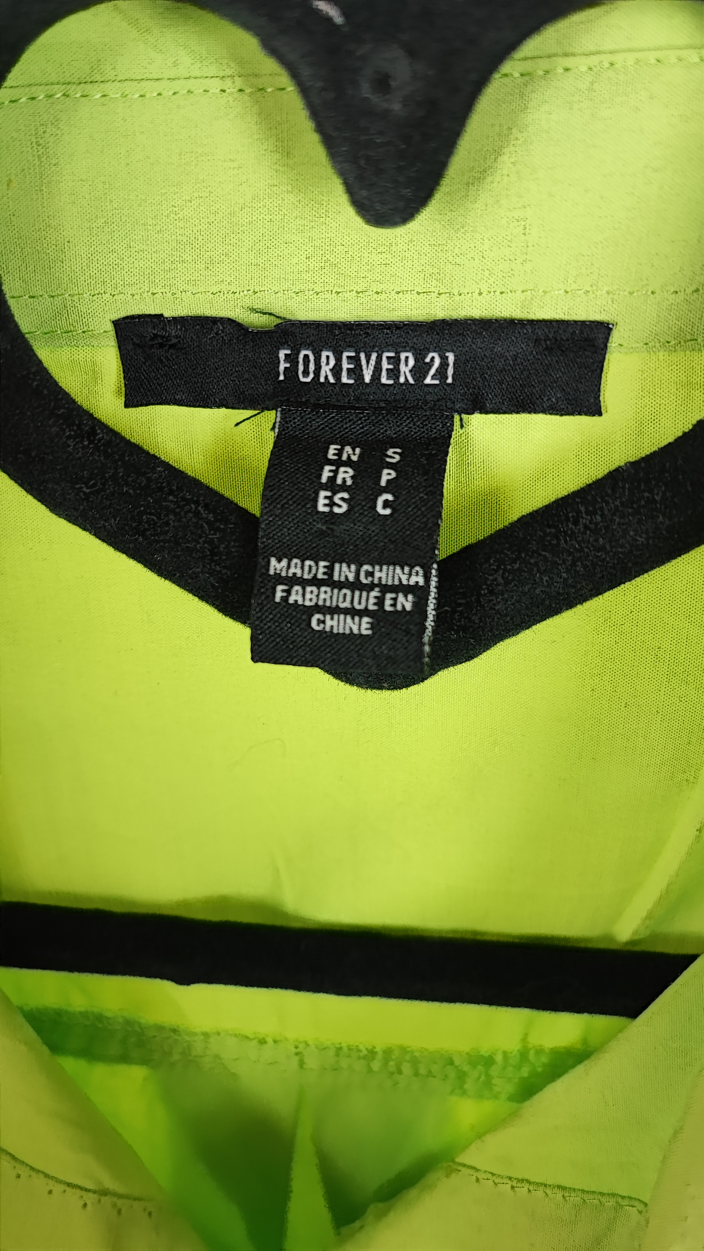 زن با شومیز لیمویی روشن آستین‌بلند و یقه برگردان دیده می‌شود. فرم لباس آزاد است و با شلوار جین تیره ست شده.»