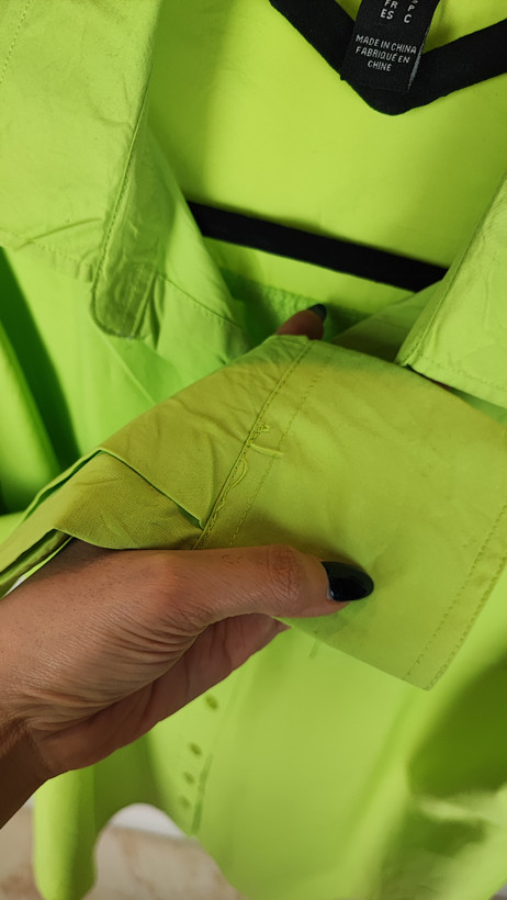 زن با شومیز لیمویی روشن آستینبلند و یقه برگردان دیده میشود. فرم لباس آزاد است و با شلوار جین تیره ست شده.»