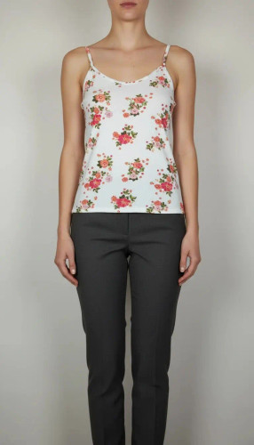 زن با تاپ بندی سفید طرحدار با فرم جذب و بندهای نازک دیده میشود. طرح لباس شامل نقشهای رنگی ملایم است و با شلوار مشکی ست شده.»