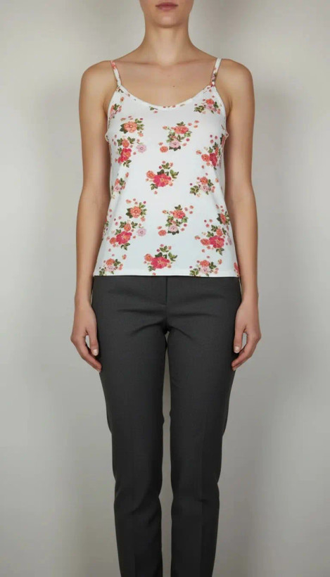 زن با تاپ بندی سفید طرحدار با فرم جذب و بندهای نازک دیده میشود. طرح لباس شامل نقشهای رنگی ملایم است و با شلوار مشکی ست شده.»