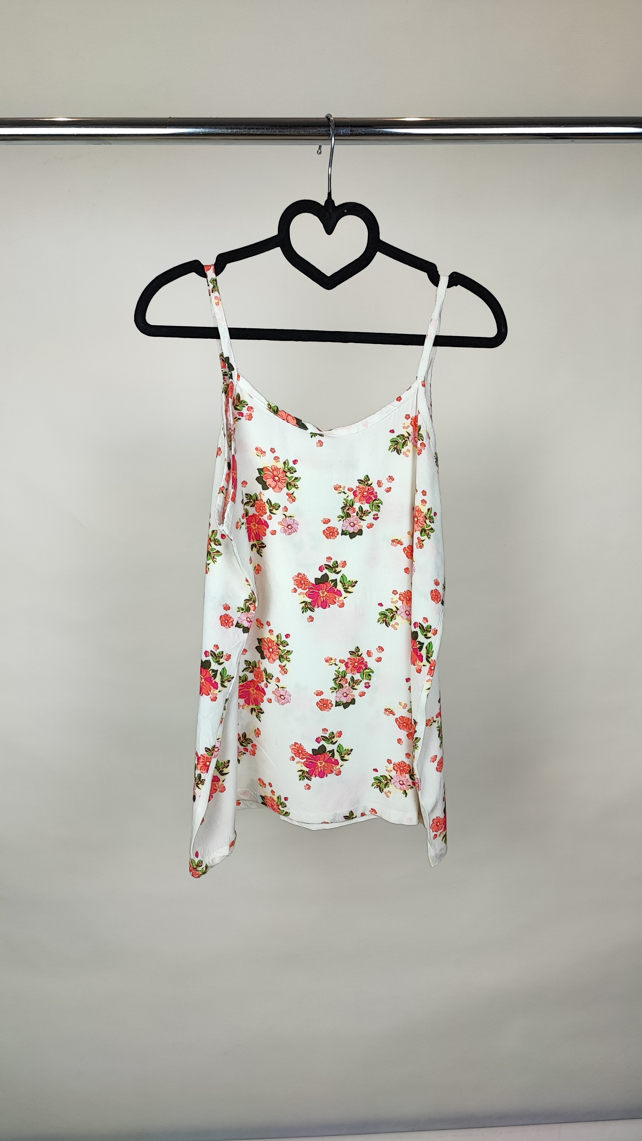 زن با تاپ بندی سفید طرحدار با فرم جذب و بندهای نازک دیده میشود. طرح لباس شامل نقشهای رنگی ملایم است و با شلوار مشکی ست شده.»