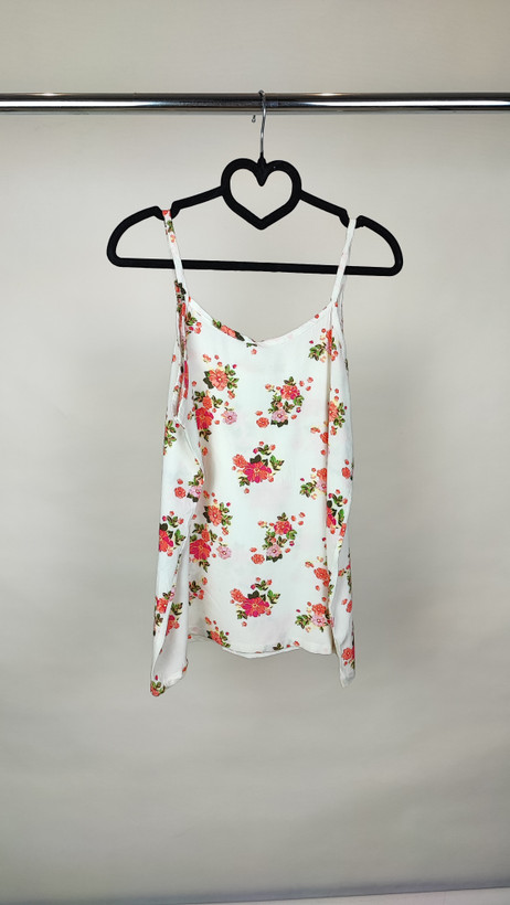 زن با تاپ بندی سفید طرحدار با فرم جذب و بندهای نازک دیده میشود. طرح لباس شامل نقشهای رنگی ملایم است و با شلوار مشکی ست شده.»