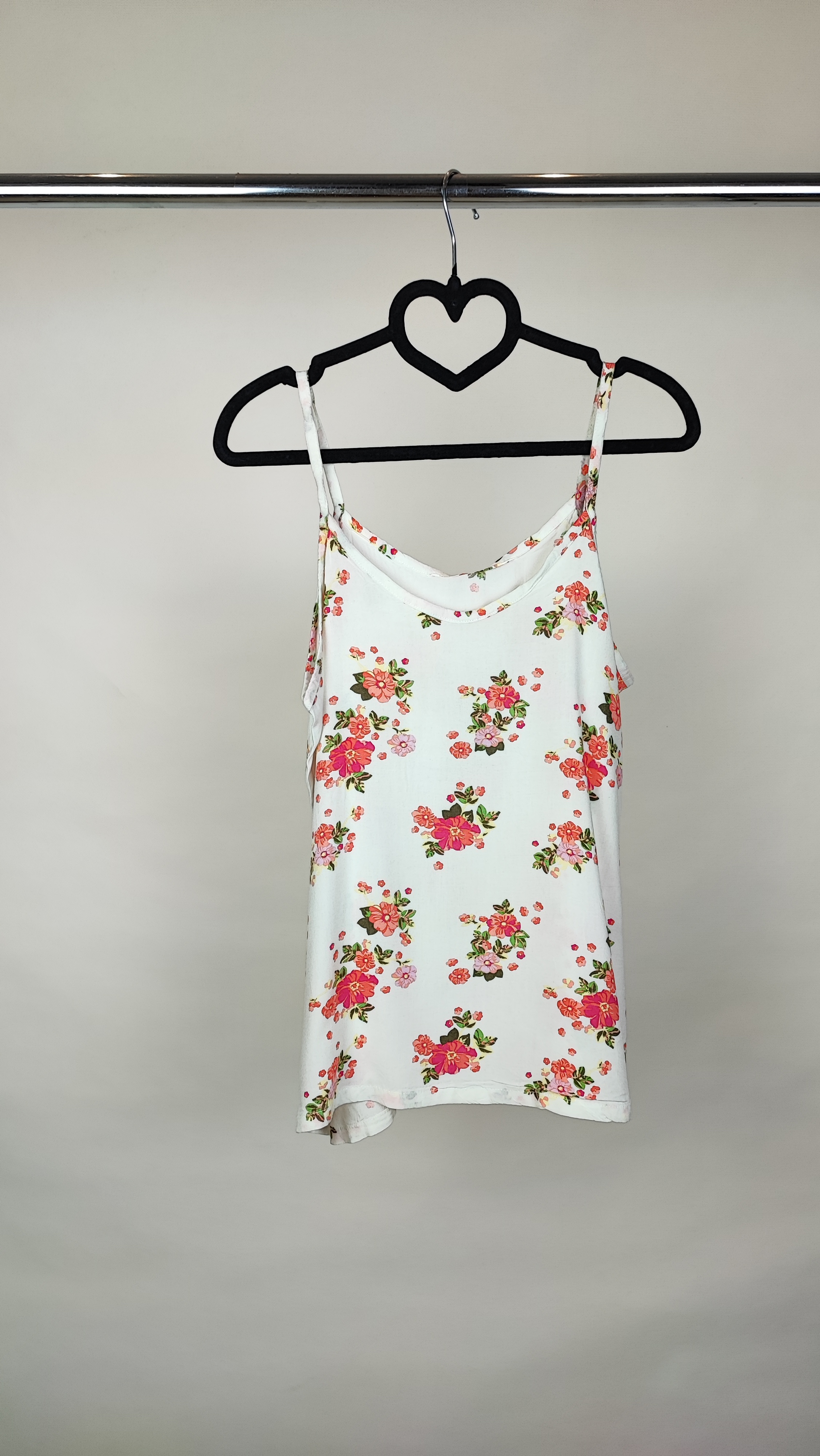 زن با تاپ بندی سفید طرحدار با فرم جذب و بندهای نازک دیده میشود. طرح لباس شامل نقشهای رنگی ملایم است و با شلوار مشکی ست شده.»