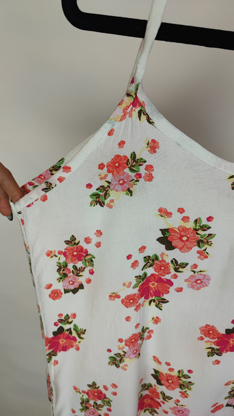 زن با تاپ بندی سفید طرحدار با فرم جذب و بندهای نازک دیده میشود. طرح لباس شامل نقشهای رنگی ملایم است و با شلوار مشکی ست شده.»