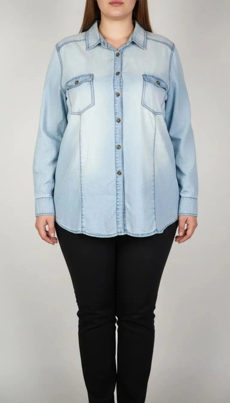 زن با شومیز جین آبی روشن سایز بزرگ و آستینبلند که جلو آن دکمهدار و دارای دو جیب سینه است، در پسزمینه روشن ایستاده.»