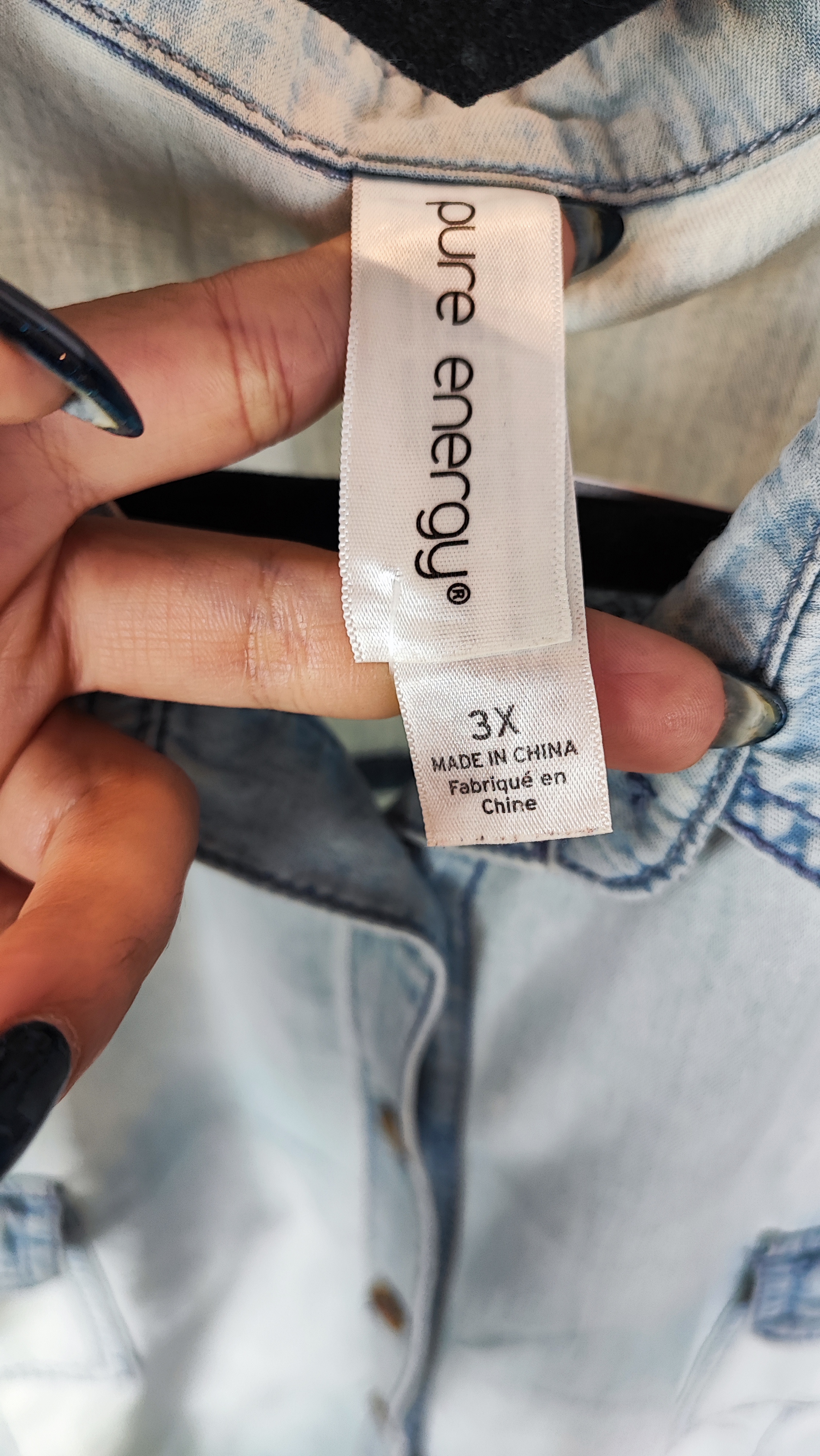 زن با شومیز جین آبی روشن سایز بزرگ و آستین‌بلند که جلو آن دکمه‌دار و دارای دو جیب سینه است، در پس‌زمینه روشن ایستاده.»