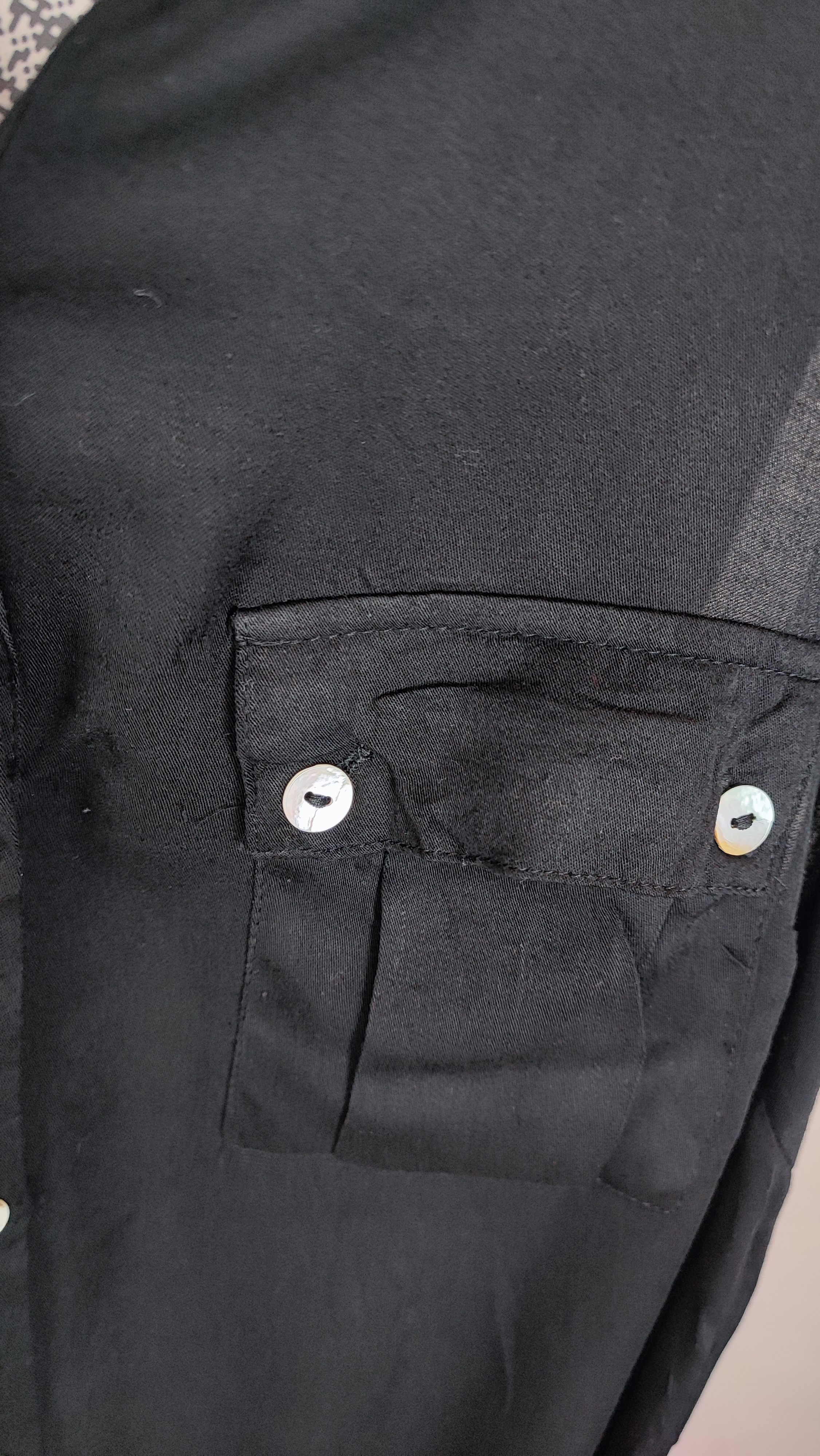 تاپ زنانه مشکی بدون آستین با دکمه‌های جلو و یقه‌برگردان روی تن مدل در پس‌زمینه روشن.»