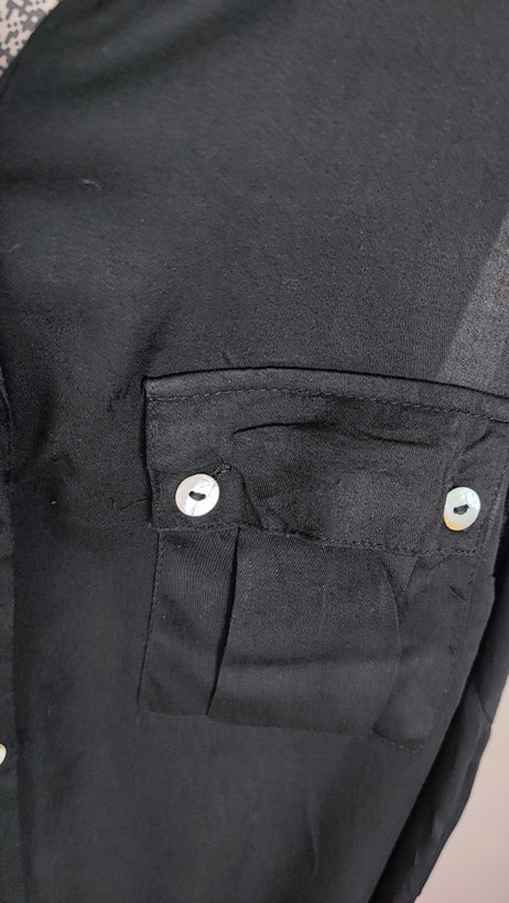 تاپ زنانه مشکی بدون آستین با دکمههای جلو و یقهبرگردان روی تن مدل در پسزمینه روشن.»