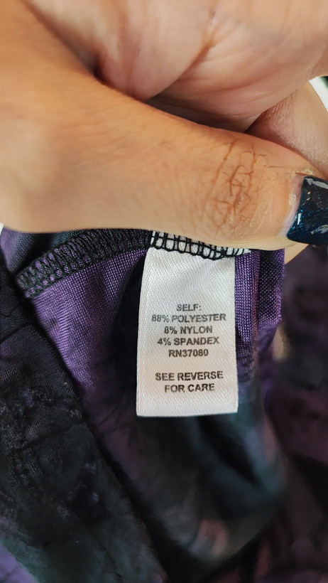 خانمی با شومیز سایز بزرگ بنفش و آبی با طرح انتزاعی، یقه آزاد و آستین سهربع، در پسزمینه روشن ایستاده است.»