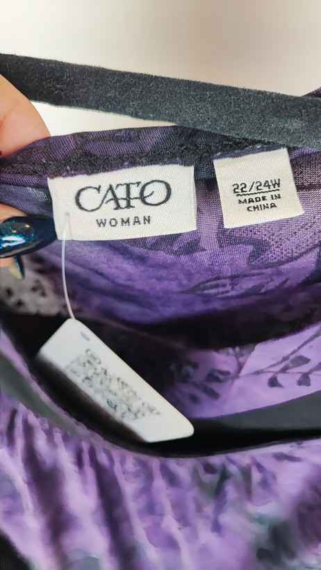 خانمی با شومیز سایز بزرگ بنفش و آبی با طرح انتزاعی، یقه آزاد و آستین سهربع، در پسزمینه روشن ایستاده است.»