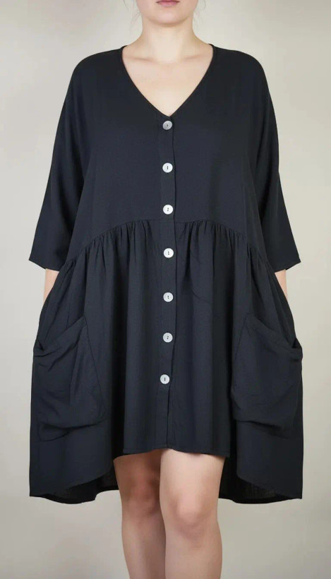 زن با تونیک مشکی سایز بزرگ، آستینکوتاه گشاد و دکمههای ردیفی در قسمت جلو، با قد تا بالای زانو، در پسزمینه روشن ایستاده است.»