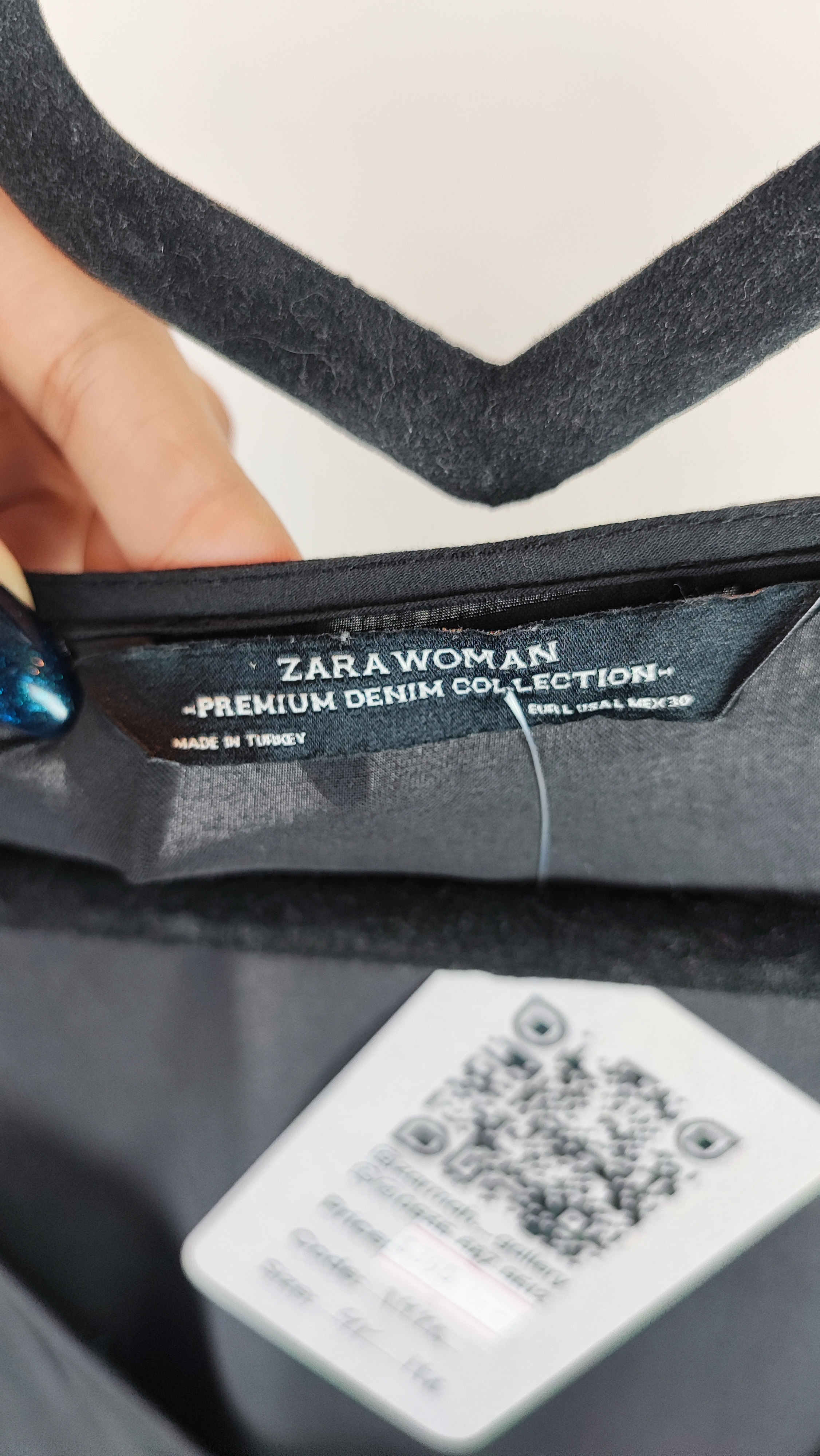 زن با تونیک مشکی سایز بزرگ، آستین‌کوتاه گشاد و دکمه‌های ردیفی در قسمت جلو، با قد تا بالای زانو، در پس‌زمینه روشن ایستاده است.»