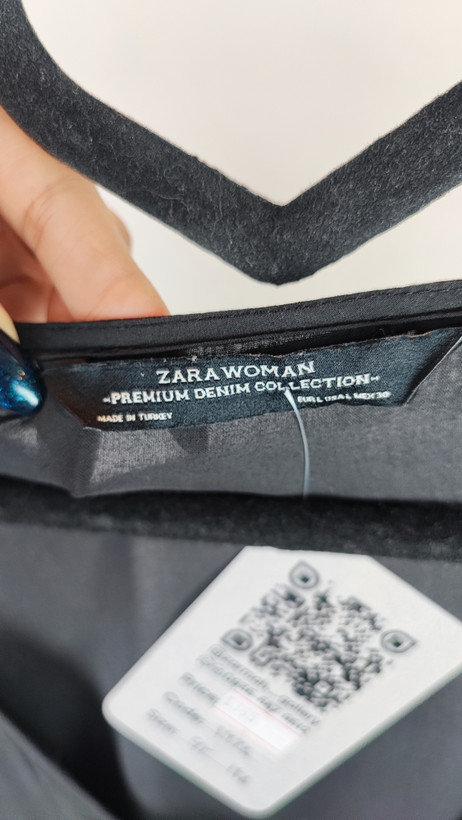 زن با تونیک مشکی سایز بزرگ، آستینکوتاه گشاد و دکمههای ردیفی در قسمت جلو، با قد تا بالای زانو، در پسزمینه روشن ایستاده است.»