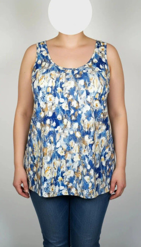 زن با تاپ زنانه سایز بزرگ طرحدار با زمینه سفید و طرحهای آبی و سبز، آستینحلقهای و یقه گرد، در پسزمینه روشن ایستاده است.»