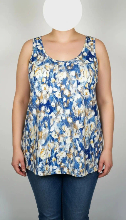 زن با تاپ زنانه سایز بزرگ طرحدار با زمینه سفید و طرحهای آبی و سبز، آستینحلقهای و یقه گرد، در پسزمینه روشن ایستاده است.»